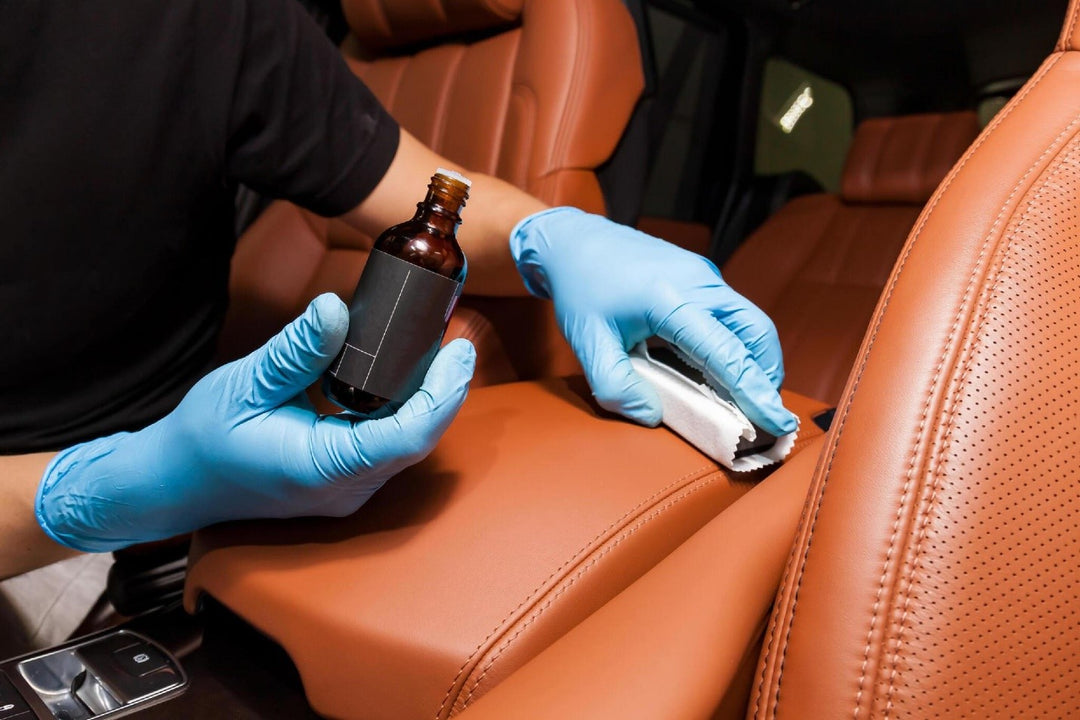 Applying a nano-ceramic coating for interior leather on the car's seat brown upholstery by a worker in blue gloves with a sponge and bottle of chemical composition. Auto service industry.