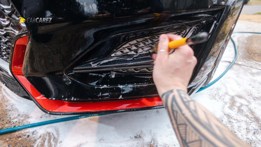 A person cleaning his car under hood with carcarez tire brush