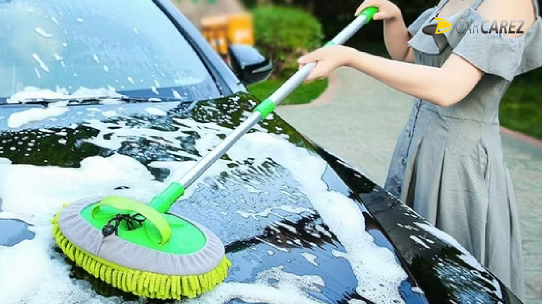 A person using a Carcarez 3-in-1 Chenille Wash Mop with an extendable pole to clean a black car covered in soap suds, demonstrating its effectiveness in reaching large surface areas.