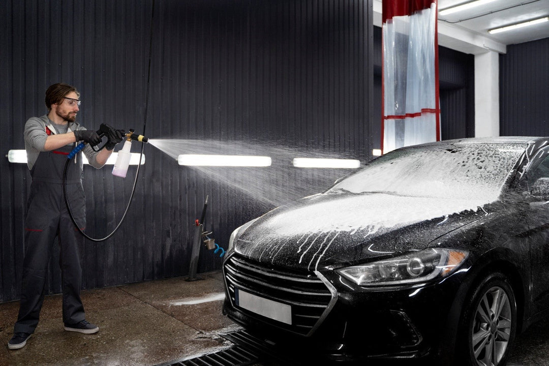 A person washing a car using a foam cannon and a soft-bristle brush, ensuring a thorough and scratch-free clean. The image highlights essential car wash tools for a professional finish.