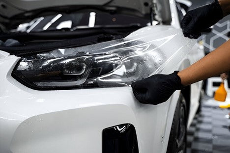 A person wearing black gloves applies a clear coat to a pristine white car, enhancing its shine and protection.