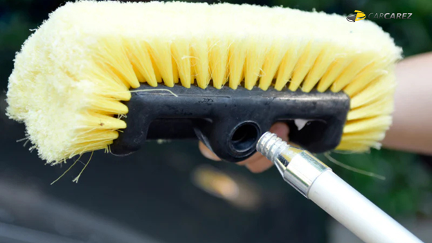 Close-up of a yellow car wash brush being attached to a handle, showing detailed bristles and connection point.