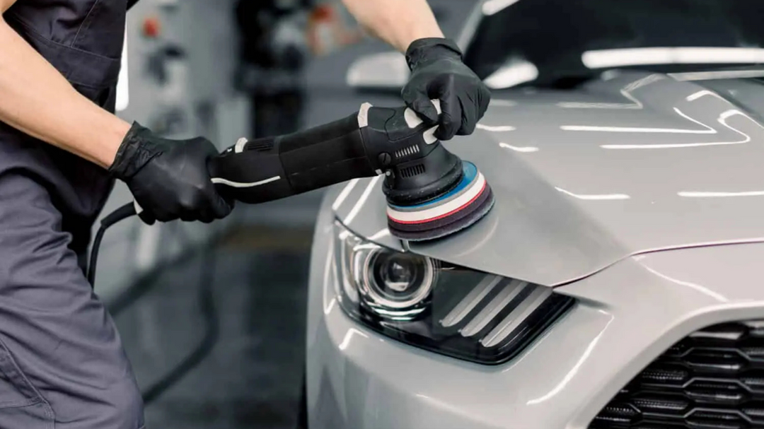Professional detailer using a dual-action polisher on the hood of a silver car for a high-gloss finish.