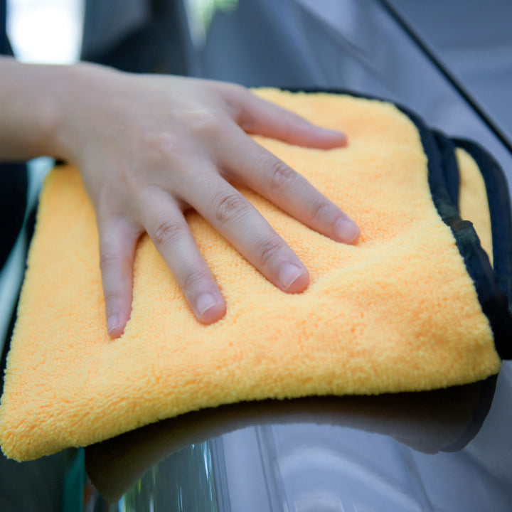 Hand holding a yellow microfiber cloth against a car window